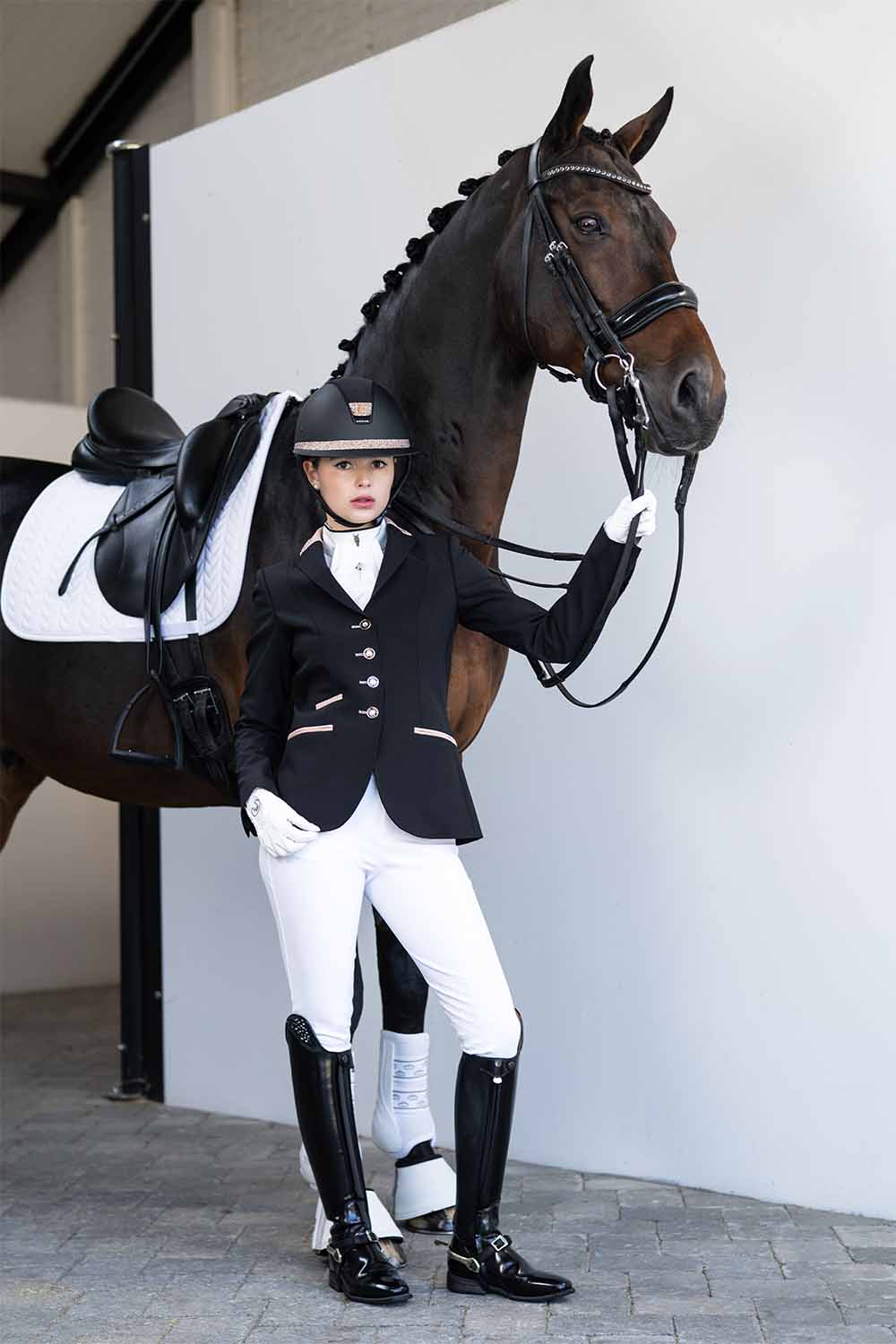 Model with horse wearing a black with pink JuulC women's competition jacket in the color Black Shimmer
