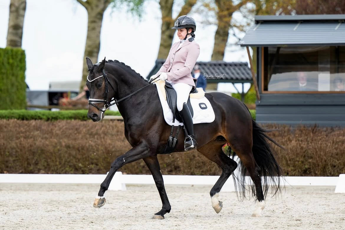 Christel Schonhoven-van Eldik riding an extended trot with her horse at a show, in a JuulC competition jacket