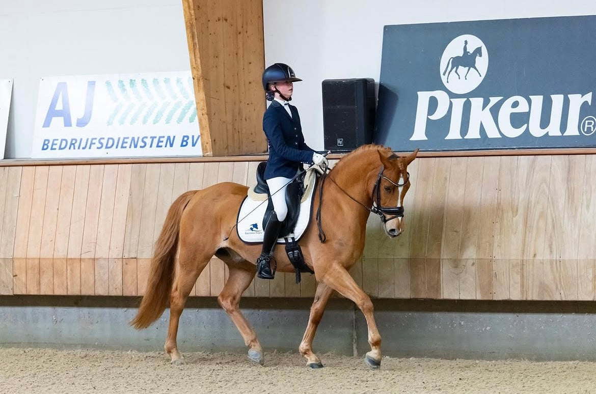 Itske van Kuijlenborg and her chestnut pony in trot at the Dutch National Championships, wearing her JuulC competition coat