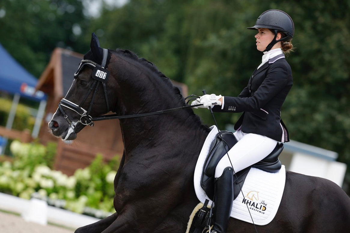Steffie Wijgergangs cantering with her black horse in their dressage competition, wearing a JuulC show coat