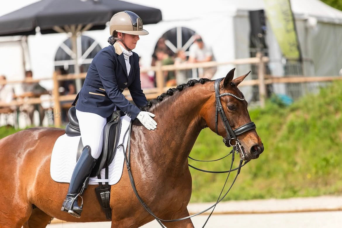 Whitney Breure rewarding her bay horse after their dressage test, in a JuulC competition coat