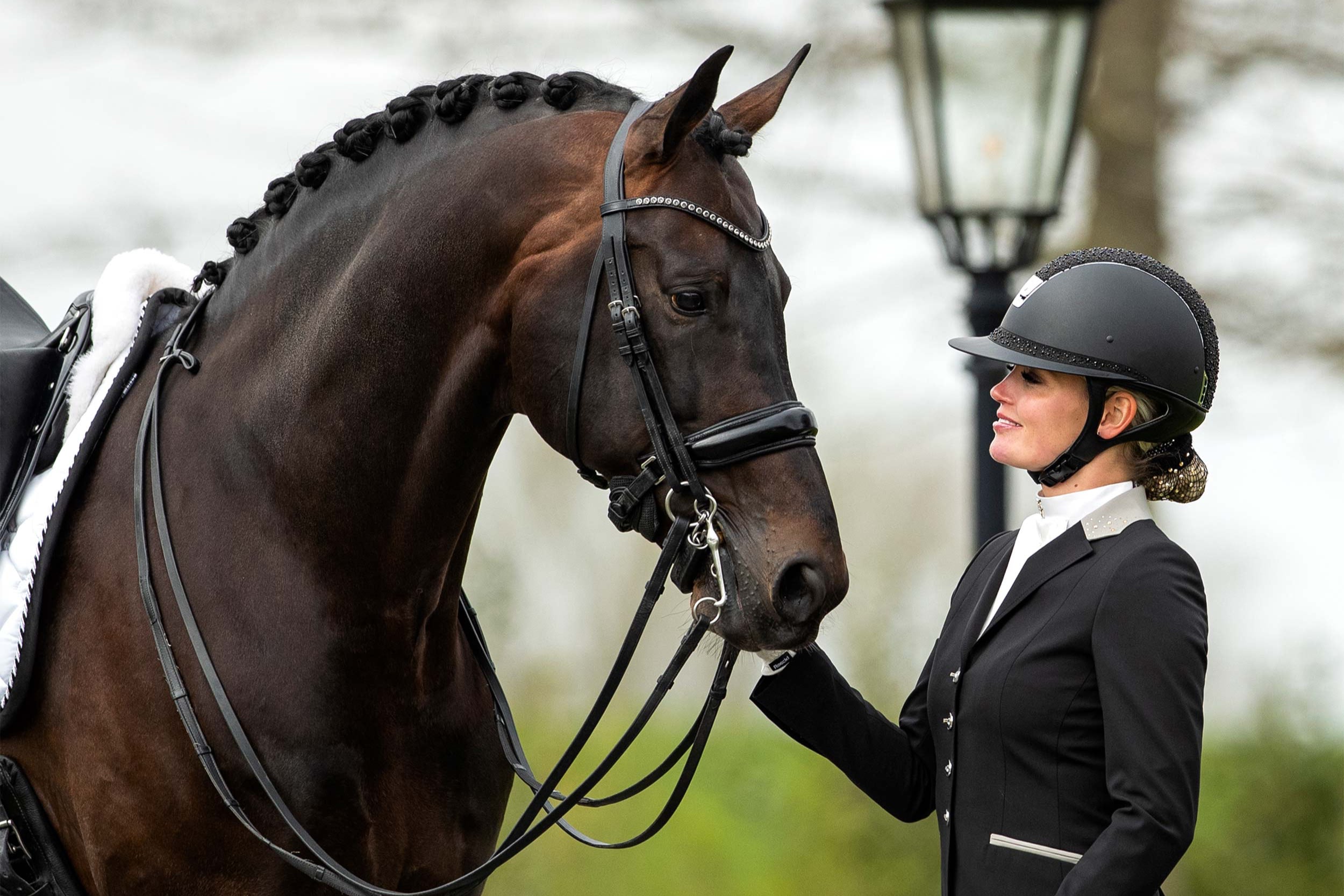 Rider touching the nose of her horse and smiling at him, in a black JuulC show coat
