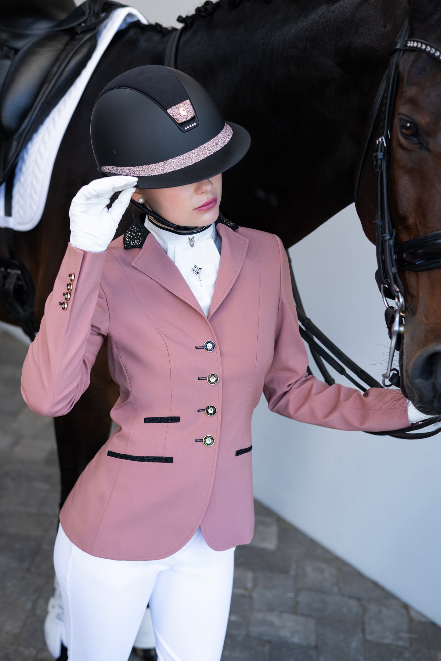 Model wearing a pink JuulC show jacket in Blush Rose while holding her horse and helmet in her hand